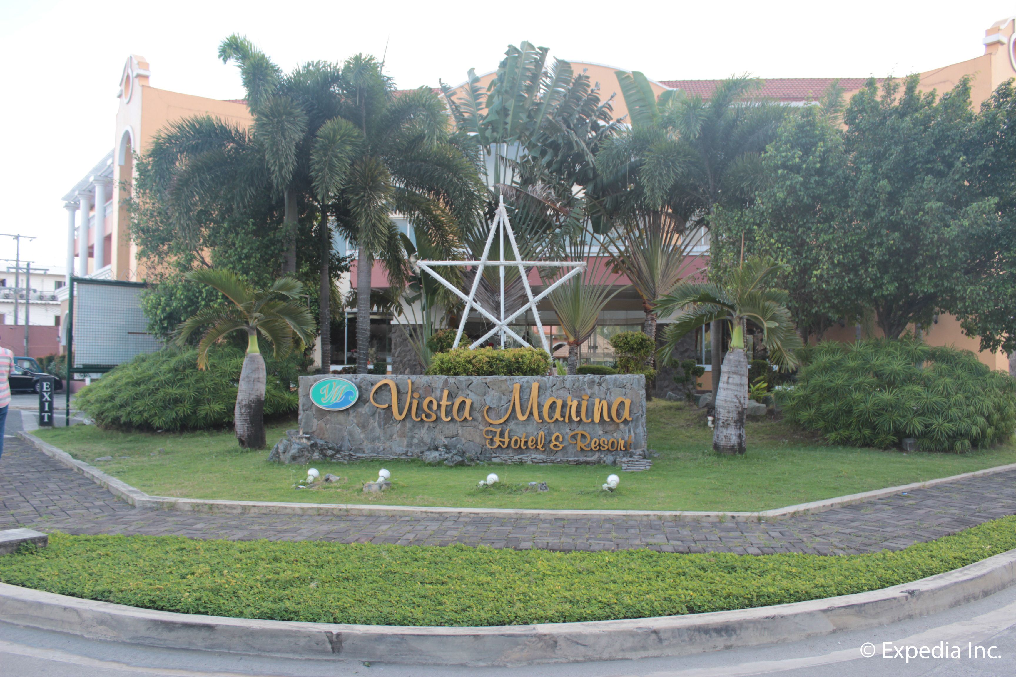 A sign for Vista Marina Hotel & Resort surrounded by greenery and palm trees.