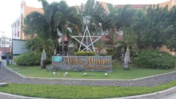 A sign for Vista Marina Hotel & Resort surrounded by greenery and palm trees.