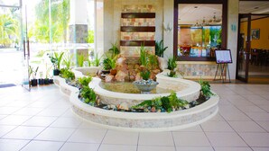 Zona de recepción con una fuente de piedra, plantas en macetas y un área de descanso.