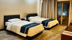 Habitación de hotel con dos camas, una mesita de noche con lámpara y un ventanal corredero que da a un balcón.