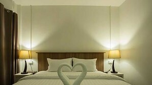 A hotel room with a neatly made bed, two bedside lamps, and a heart-shaped towel arrangement on the bed. - A Plus Hotel Koh Lipe - Hostel (Koh Lipe)