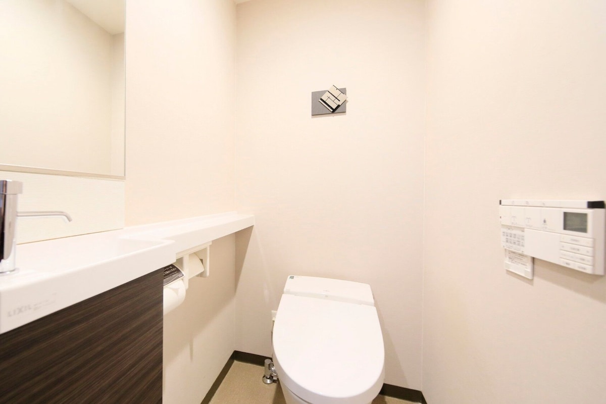 Une petite salle de bain moderne avec un lavabo blanc, des toilettes et un panneau de commande fixé au mur.