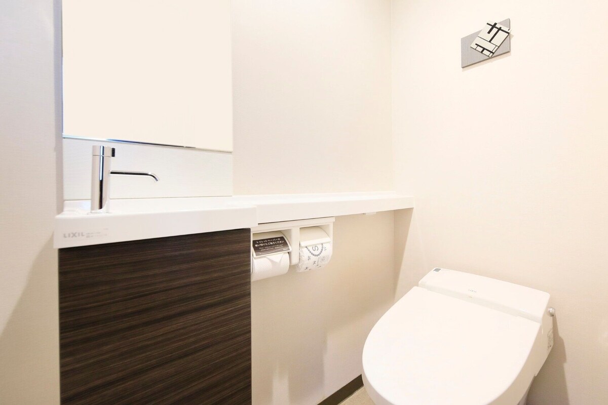 Une salle de bain moderne avec des toilettes blanches, un lavabo avec un robinet et un miroir.