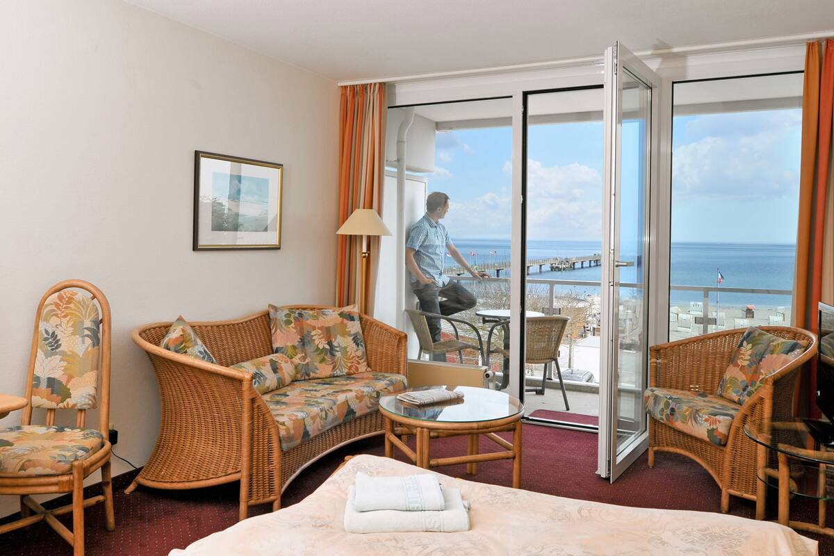 Ein Hotelzimmer mit Balkon, Korbmöbeln, einem Bett und Meerblick.