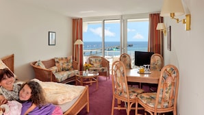 Habitación de hotel con un ventanal grande, muebles de mimbre, una mesa de comedor y un televisor.
