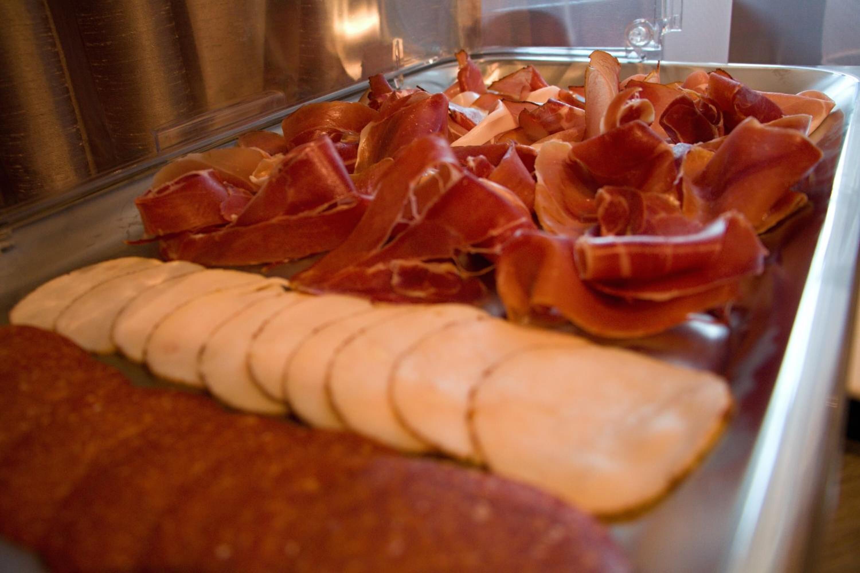 A glass display case with sliced cured meats and cheese.