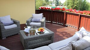 A covered outdoor seating area with wicker furniture and a glass table with fruit and wine glasses.