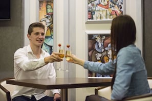 Dos personas brindando en una mesa, con un cuadro al fondo.
