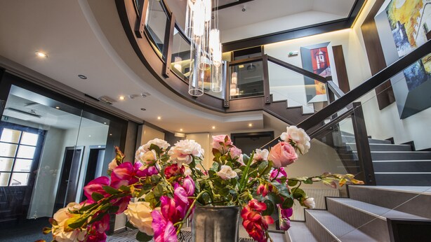 A modern interior with a staircase, a metal vase with flowers, and a large window.