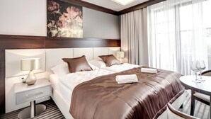 A modern hotel room with a large bed, two bedside lamps, a small table with a glass, and a painting on the wall.