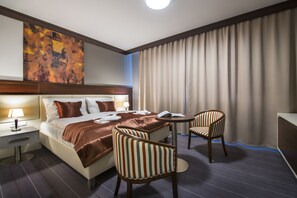 A hotel room with a large bed, two striped chairs, a small table, and a large abstract painting on the wall. - Boutique Hotel Villa ZAUBER (Poprad)