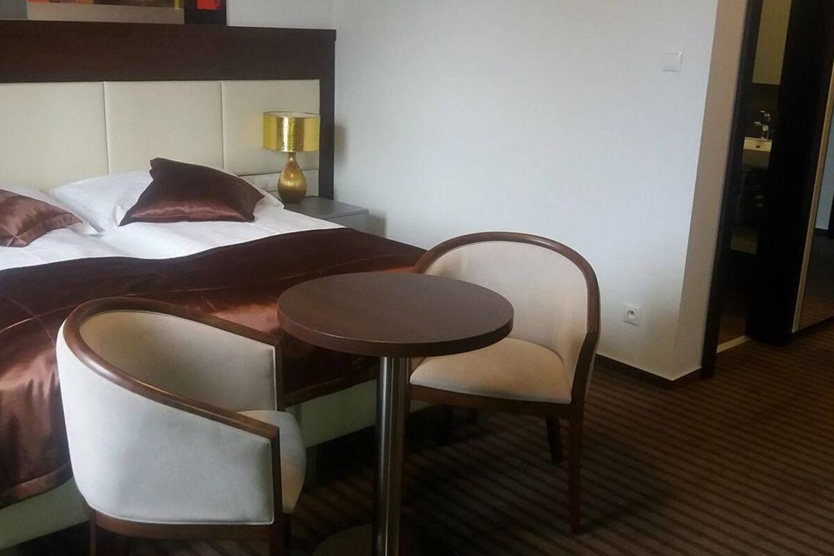 A hotel room with a bed, two armchairs, a small round table, and a nightstand with a lamp.