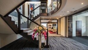 A modern hotel lobby with a curved staircase, a reception desk, and a dining area.