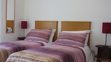 Une chambre double avec deux lits, chacun doté de draps à rayures et d’une tête de lit en bois. On y trouve des tables de chevet avec des lampes et un miroir au mur.