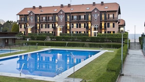A residential building with a swimming pool, a well-maintained lawn, and a paved walkway. - Abba Comillas Apartments (Comillas)