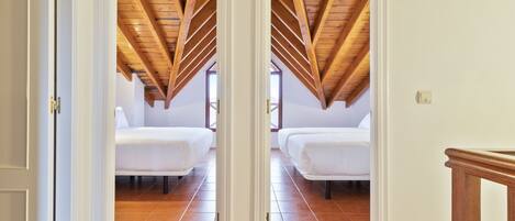 Une chambre avec deux lits, des poutres apparentes en bois au plafond et un sol carrelé.