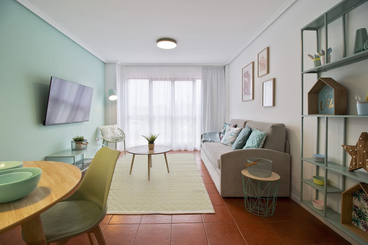 Una sala moderna con un sofá, un televisor montado en la pared, una mesa de comedor con sillas y una estantería.