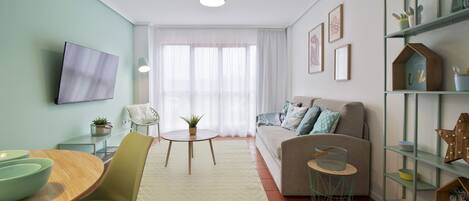 Uma sala de estar moderna com um sofá, uma TV fixada na parede, uma mesa de jantar com cadeiras e uma estante de livros.