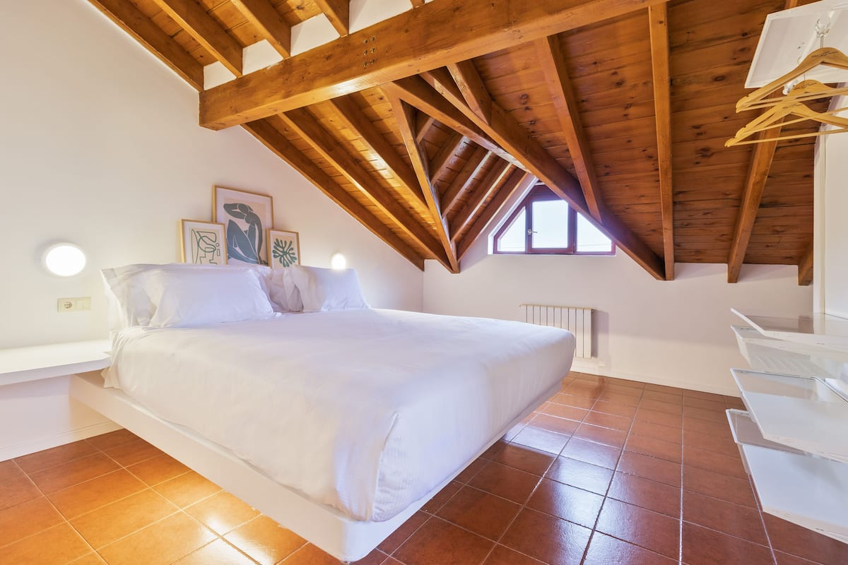 Un dormitorio con techo de madera, una cama, un radiador y una ventana.