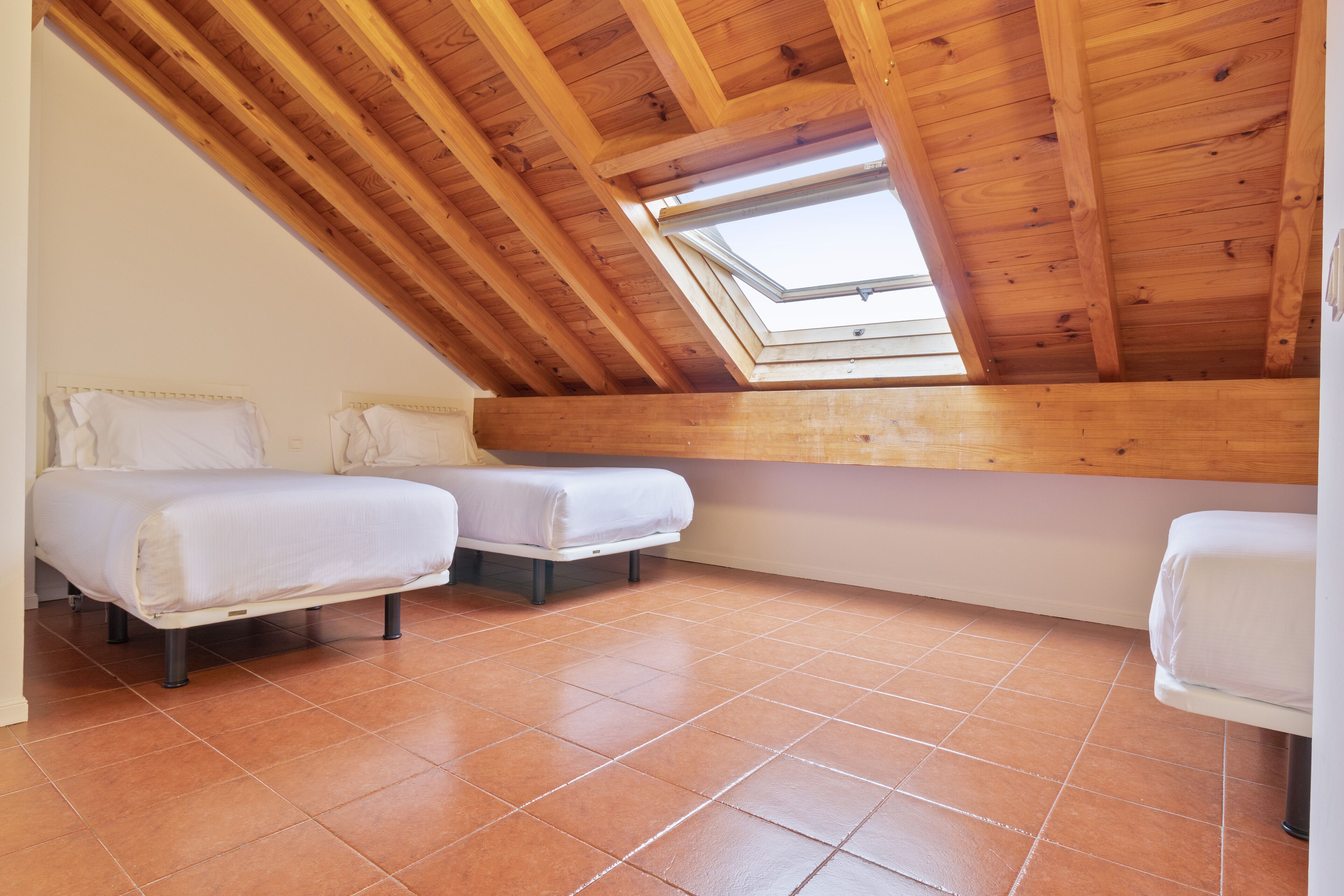 Una habitación pequeña con techo inclinado, dos camas y un tragaluz.