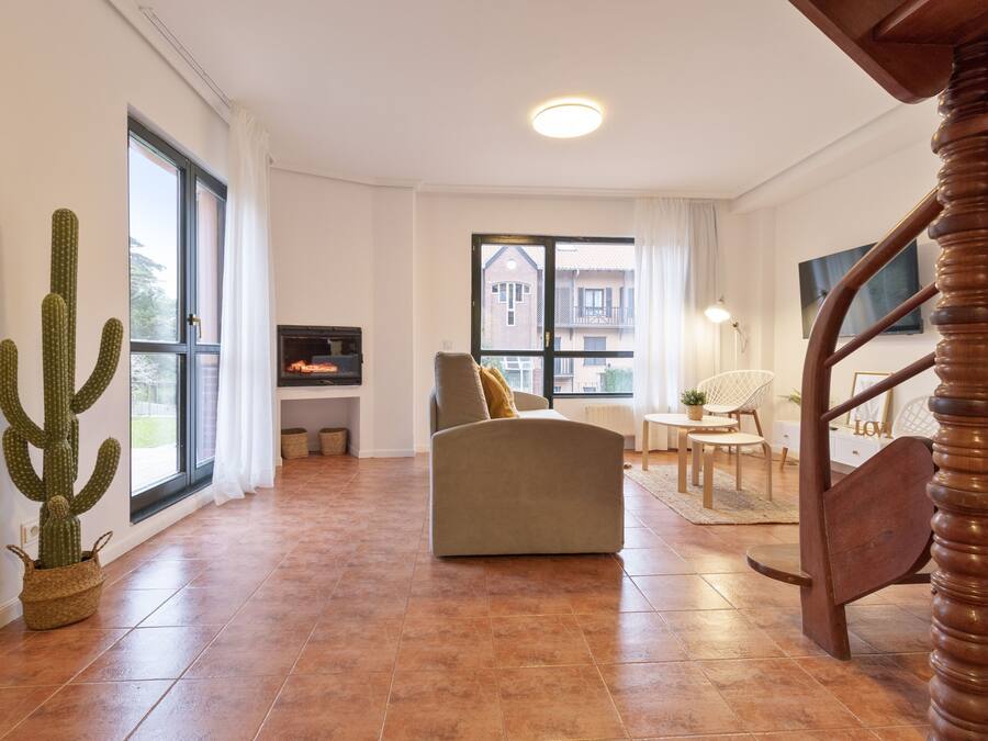 Un salón amplio con un ventanal grande, un sofá, una escalera de madera y una planta de cactus.