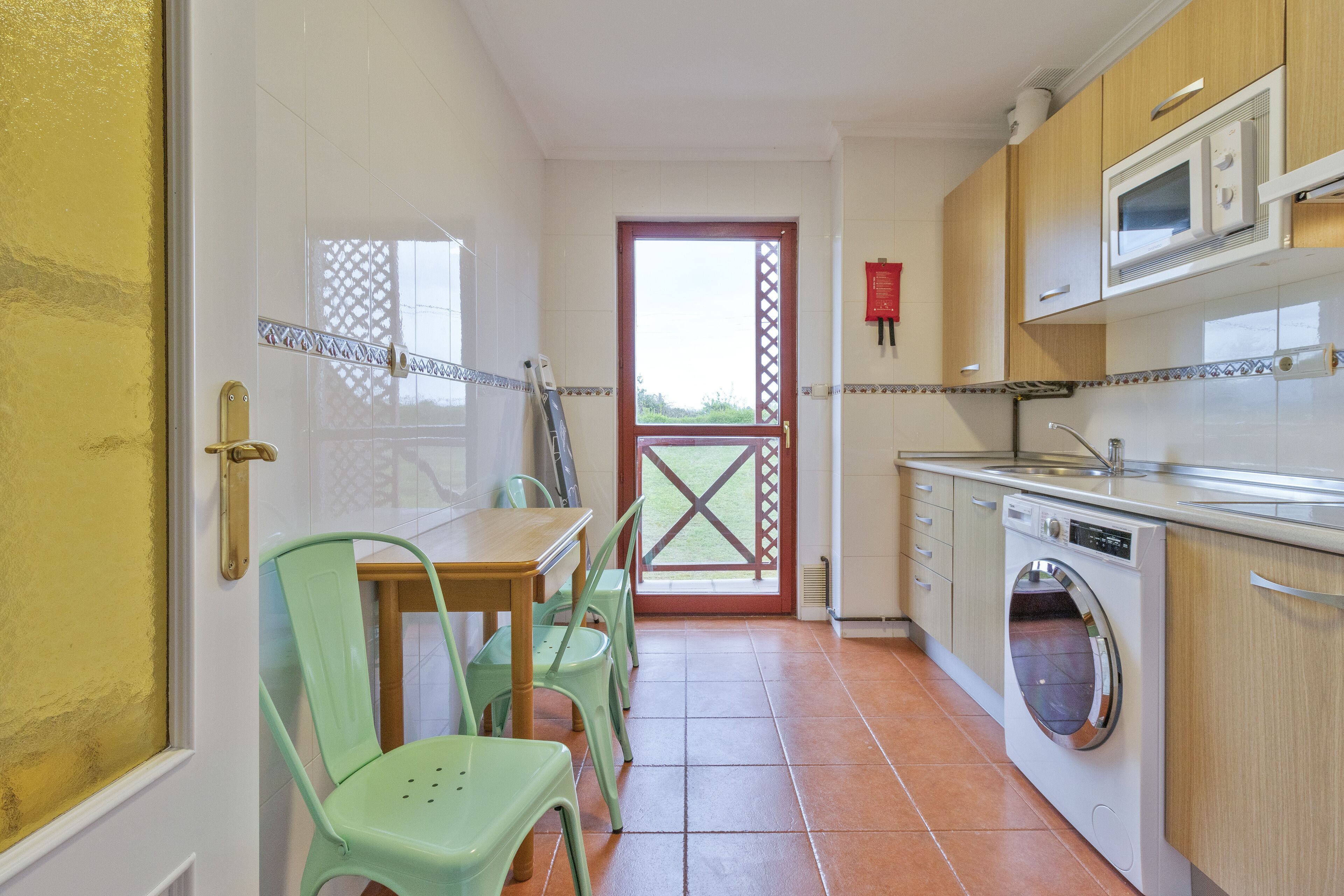 Cocina compacta con lavadora, mesa de comedor con sillas y vista a través de una puerta.