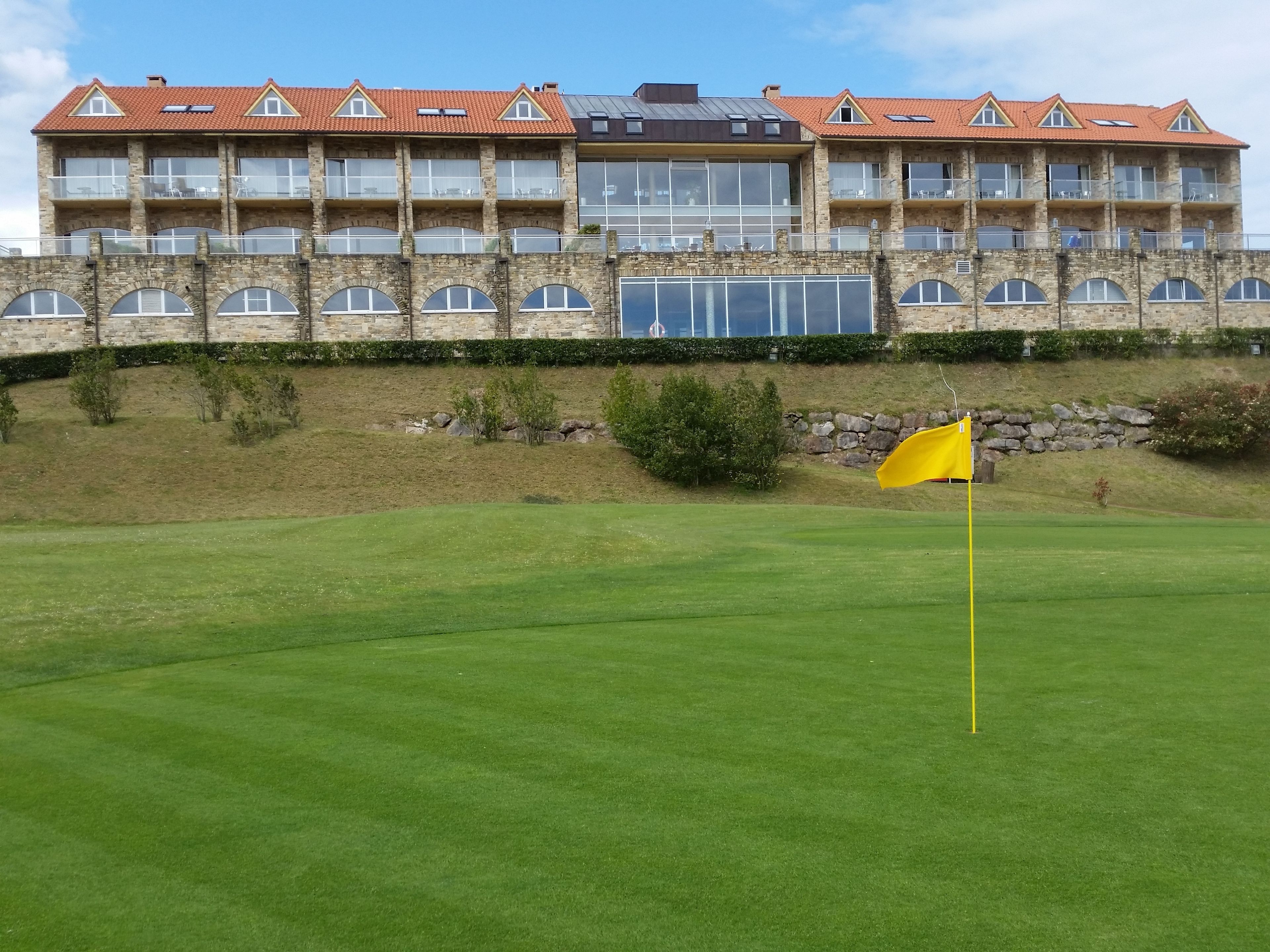 A building with multiple balconies and large windows, a stone facade, and a flag on a green field.