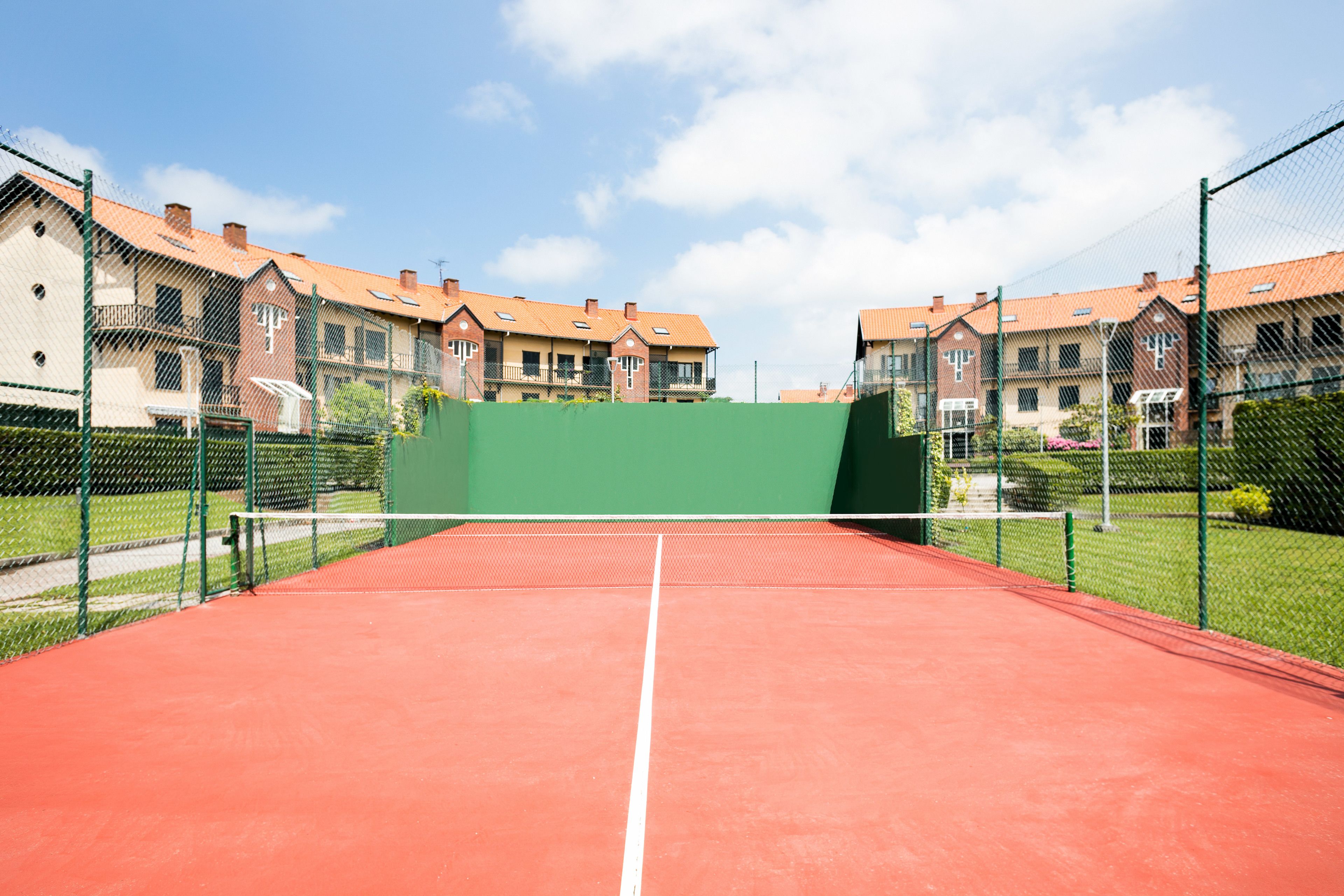 Een tennisbaan met een groene achtergrond, omringd door woongebouwen met rode daken.