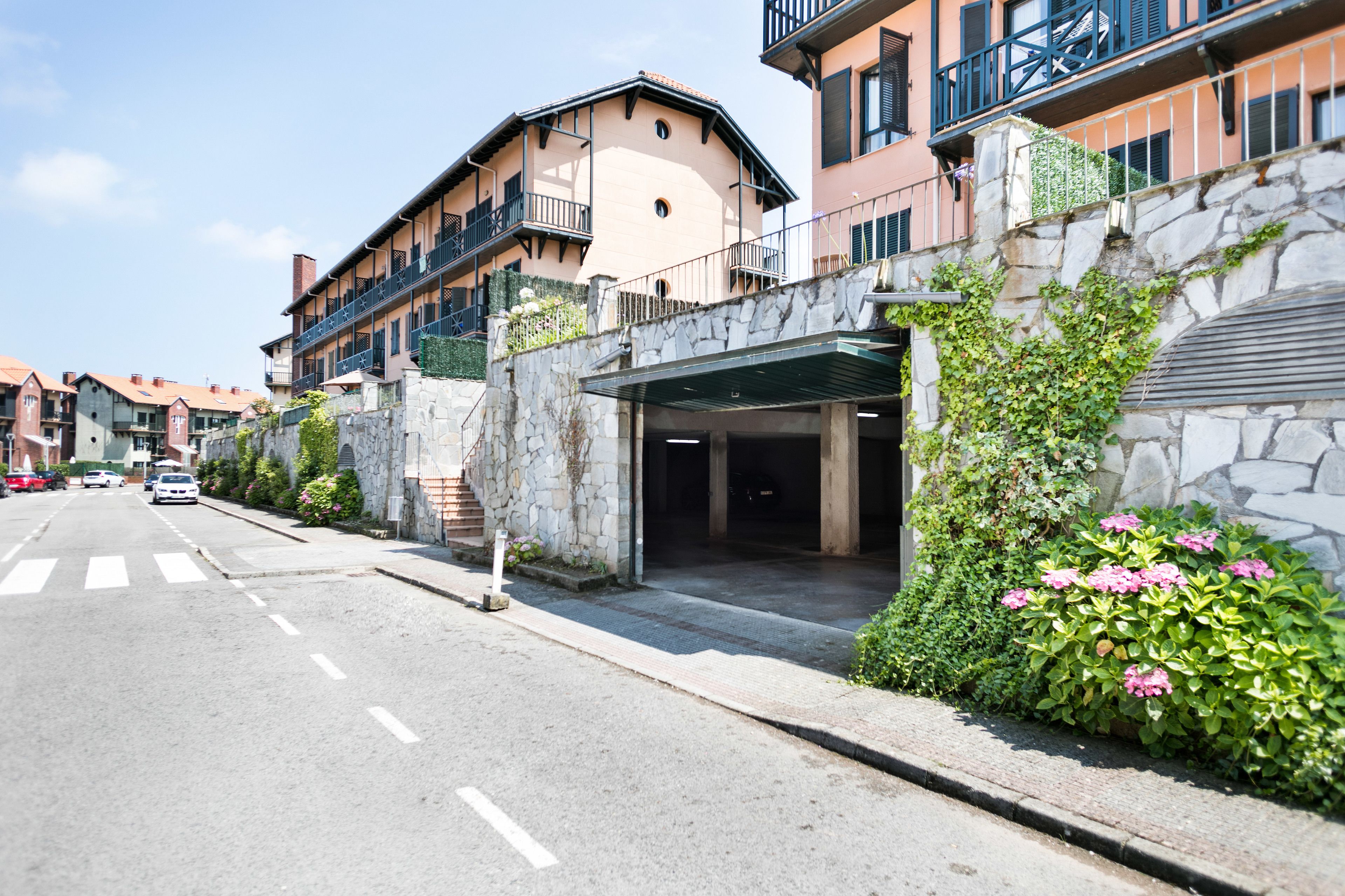 Une vue de rue d’un immeuble avec une façade en pierre, une entrée abritée et une route dégagée devant.