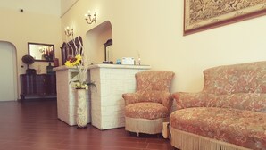 A reception area with a white reception desk, a large mirror, and a floral-patterned sofa. - Airport Rooms Bari  (Bari)
