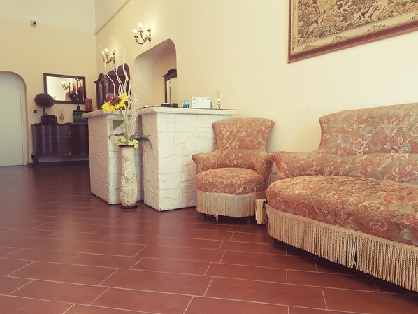 A reception area with a white reception desk, a large mirror, and a floral-patterned sofa. - Airport Rooms Bari  (Bari)