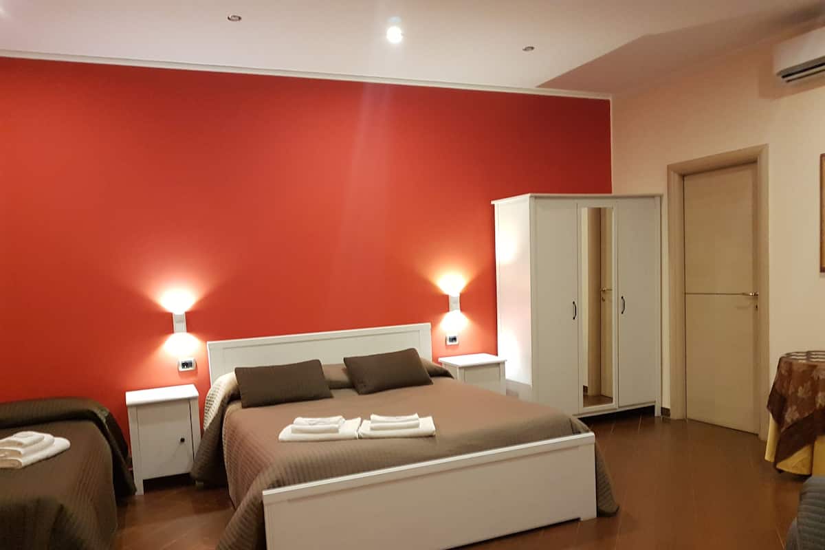 A bedroom with a large bed, two bedside tables, a wardrobe, and a small table with a tablecloth.