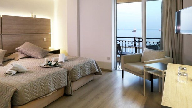 Ein Hotelzimmer mit zwei Betten, einem Balkon mit Blick und einem Schreibtisch sowie einem Fernseher.