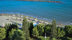 Ein Strand mit Liegestühlen und Sonnenschirmen, ein steiniger Wellenbrecher und ein klares, blaues Meer.