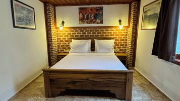 A room with a wooden ceiling, a brick wall, a bed with white bedding, and a chandelier.