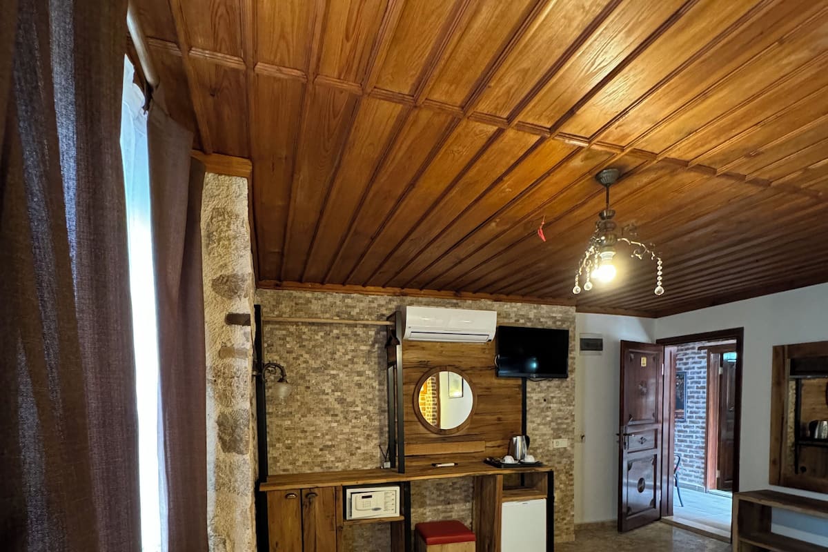 A cozy room with a wooden ceiling, a stone wall, a television, a small kitchenette, and a bed.