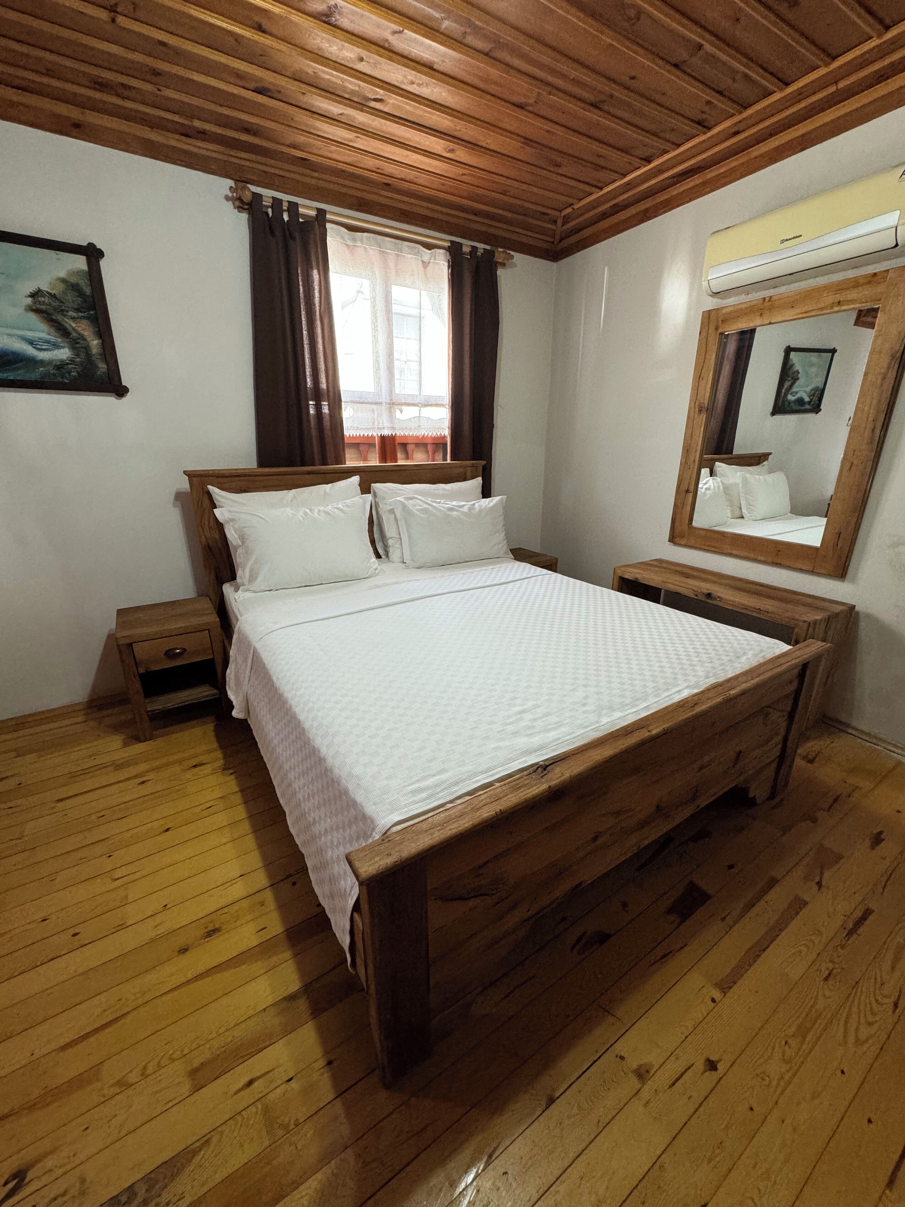 A wooden-framed bed with white linens in a room with wooden flooring and a wooden ceiling.