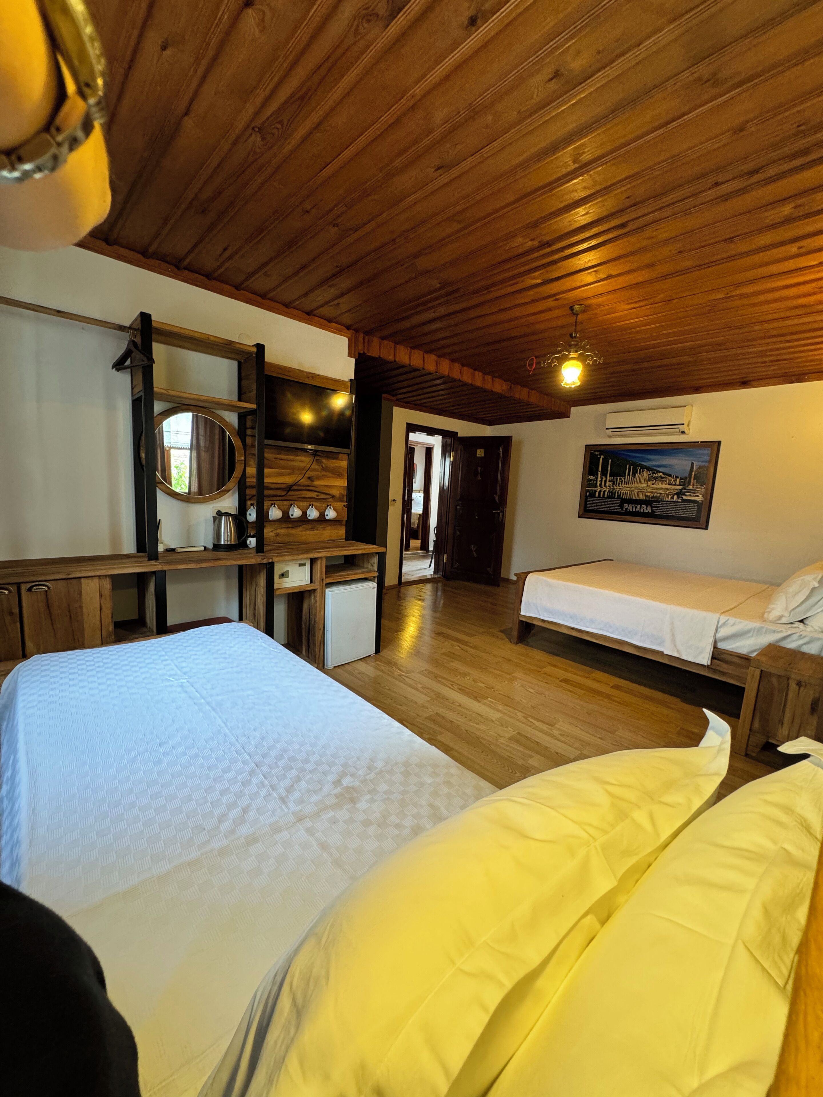 Habitación con dos camas, piso de madera, un espejo, un refrigerador pequeño, un escritorio y un cuadro en la pared.