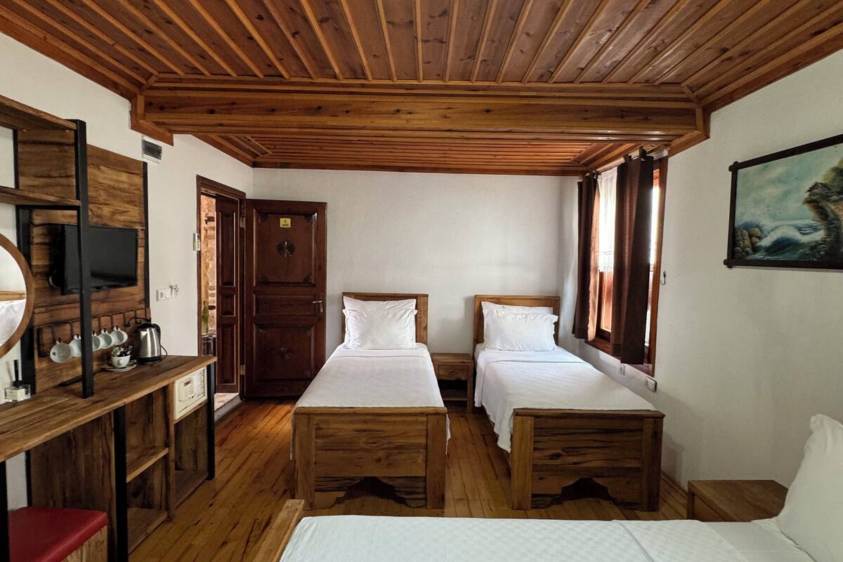 A room with wooden ceiling beams, two single beds, a wooden desk with a television, and a painting on the wall.