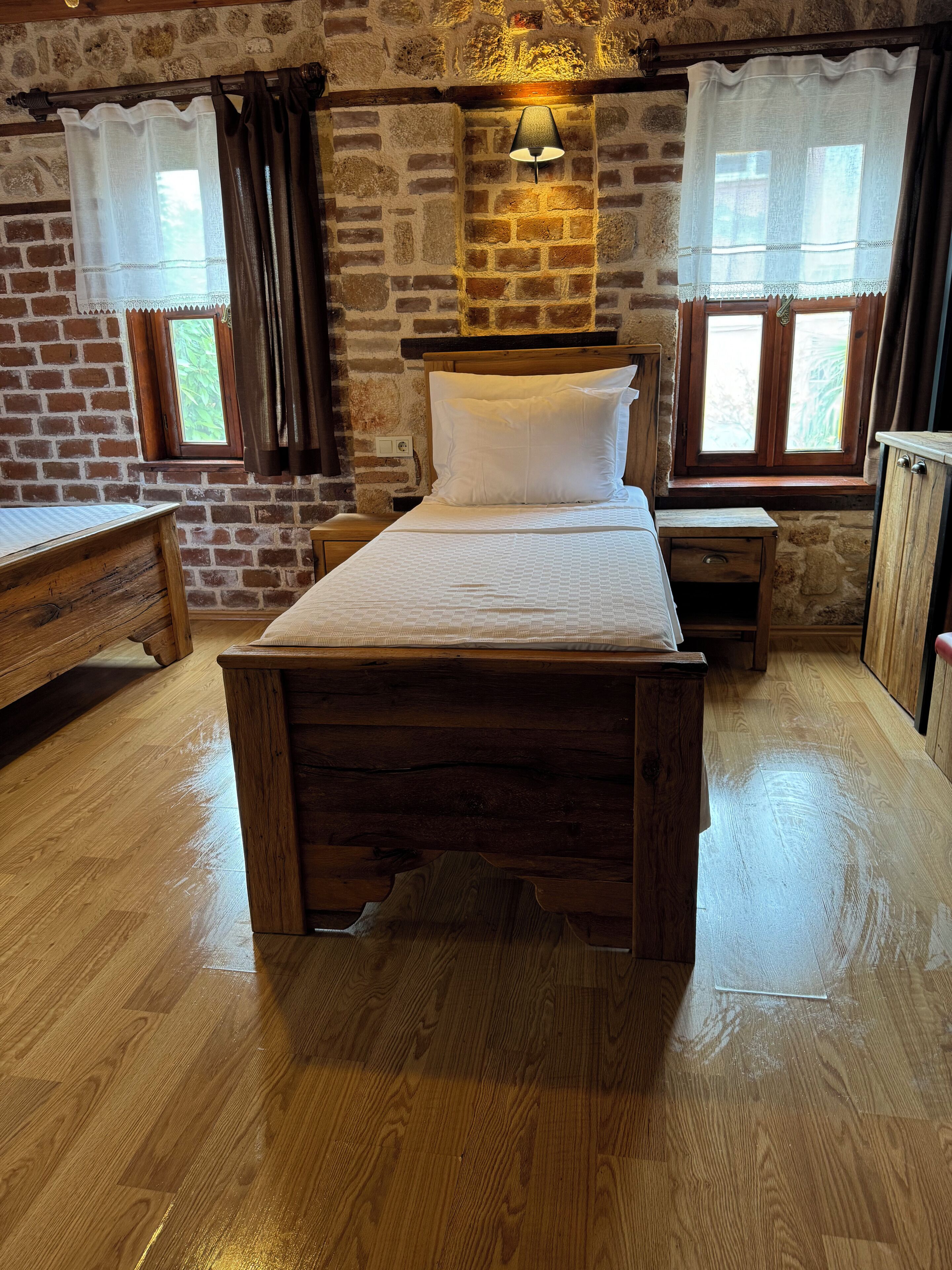 Una habitación con una cama de madera, una mesita de noche, un banco y una pared de piedra.