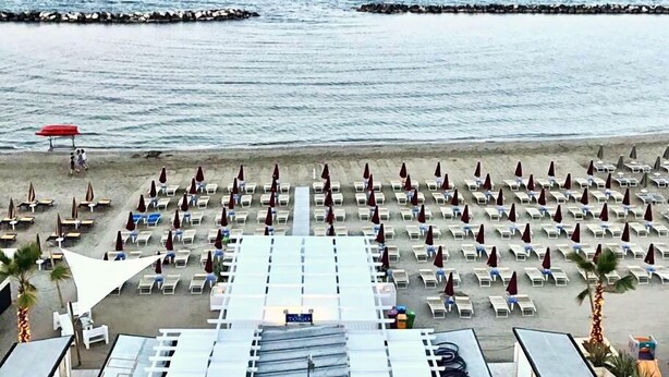 A beach with rows of sun loungers and umbrellas, a pier in the background, and a sign that reads "TOGO". - Hotel Tokio Home-Tokio Beach dependence (Ravenna)