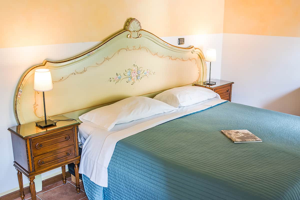 A neatly made bed with a green quilt, two bedside lamps, and a small wooden nightstand with drawers.