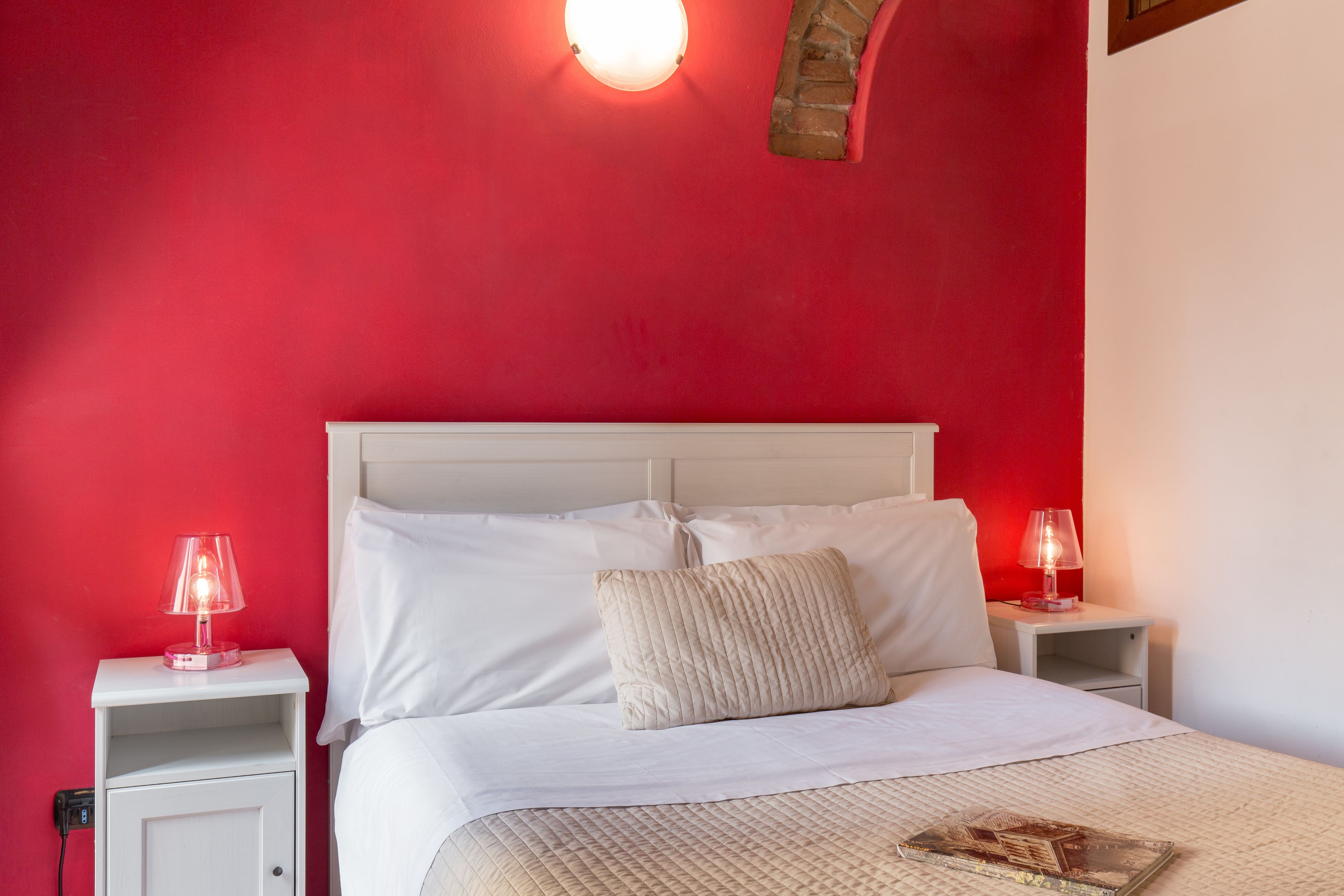 A bed with white linens and a quilted cover, two bedside lamps, a nightstand, and a wall-mounted light fixture.
