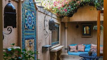 Un patio con suelo de mosaicos, un banco de madera, una mesa y un sofá con cojines.