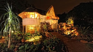 A two-story house with a thatched roof, surrounded by a landscaped garden with a water feature.