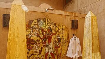 A bathroom with a mural of ancient Egyptian figures, a white robe hanging, and a tall pillar.
