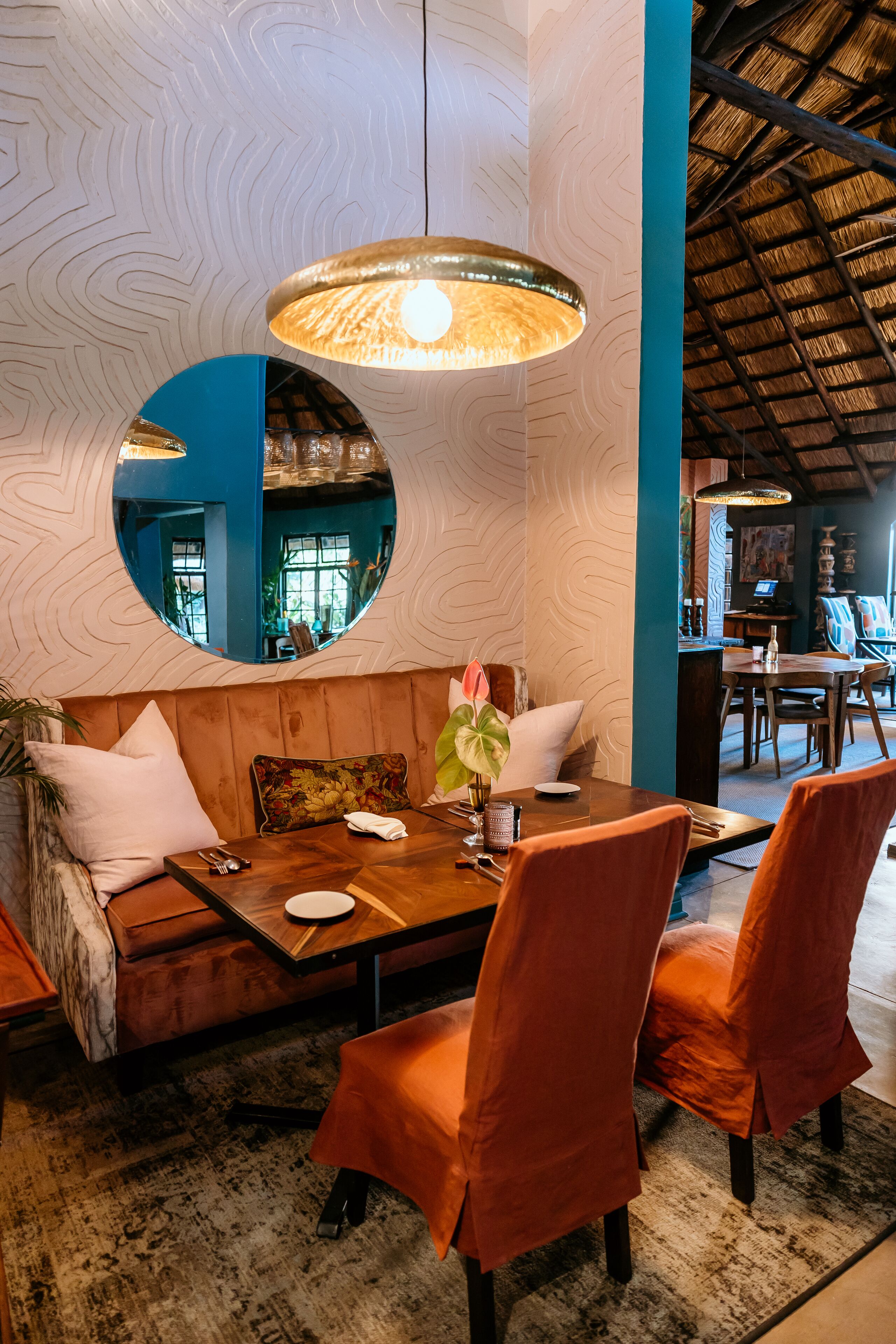 Un comedor acogedor con una mesa de madera, sillas anaranjadas y un espejo redondo en la pared.