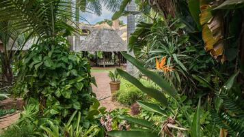 A lush garden with a thatched-roof structure, surrounded by dense tropical foliage.