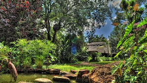 A lush garden with a pond, rocks, and a thatched-roof structure.