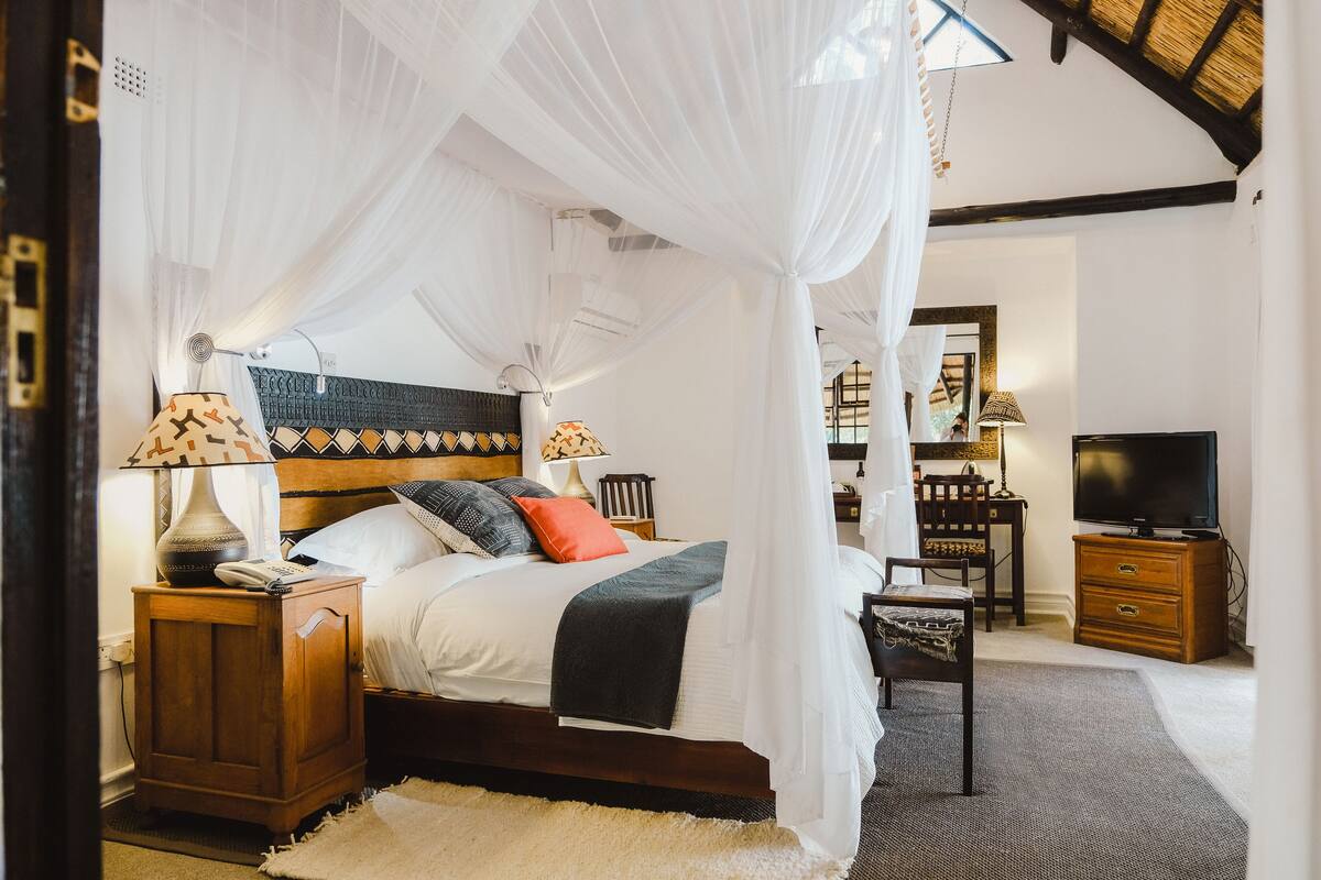 Quarto com cama de dossel, luminárias de cabeceira, televisão e mesa de cabeceira de madeira.